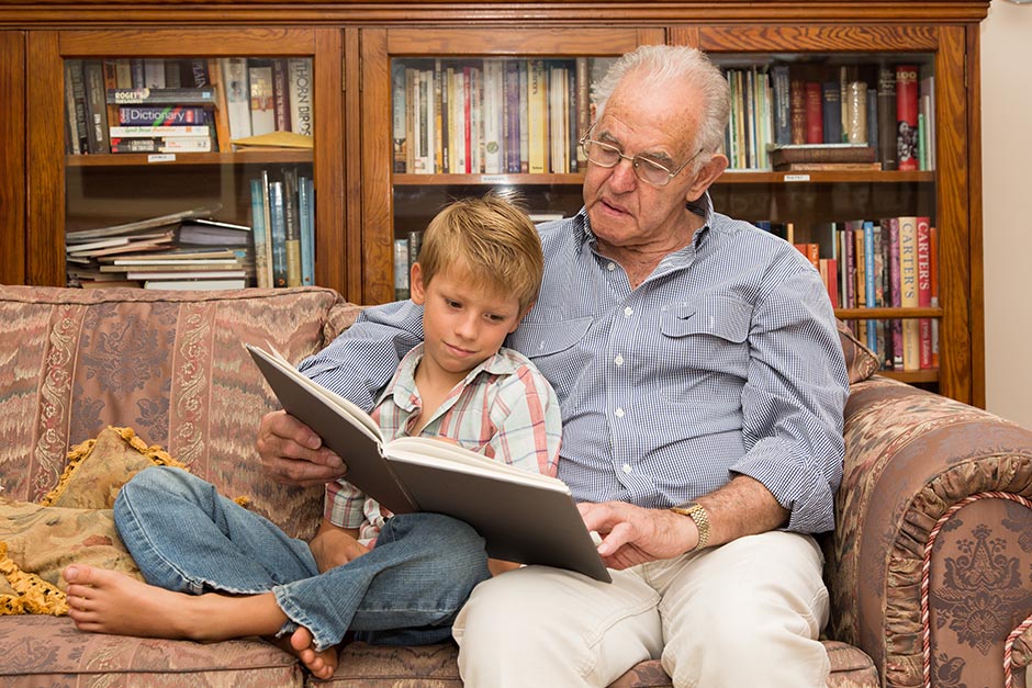 Photo of a child reading a book with his grandfather