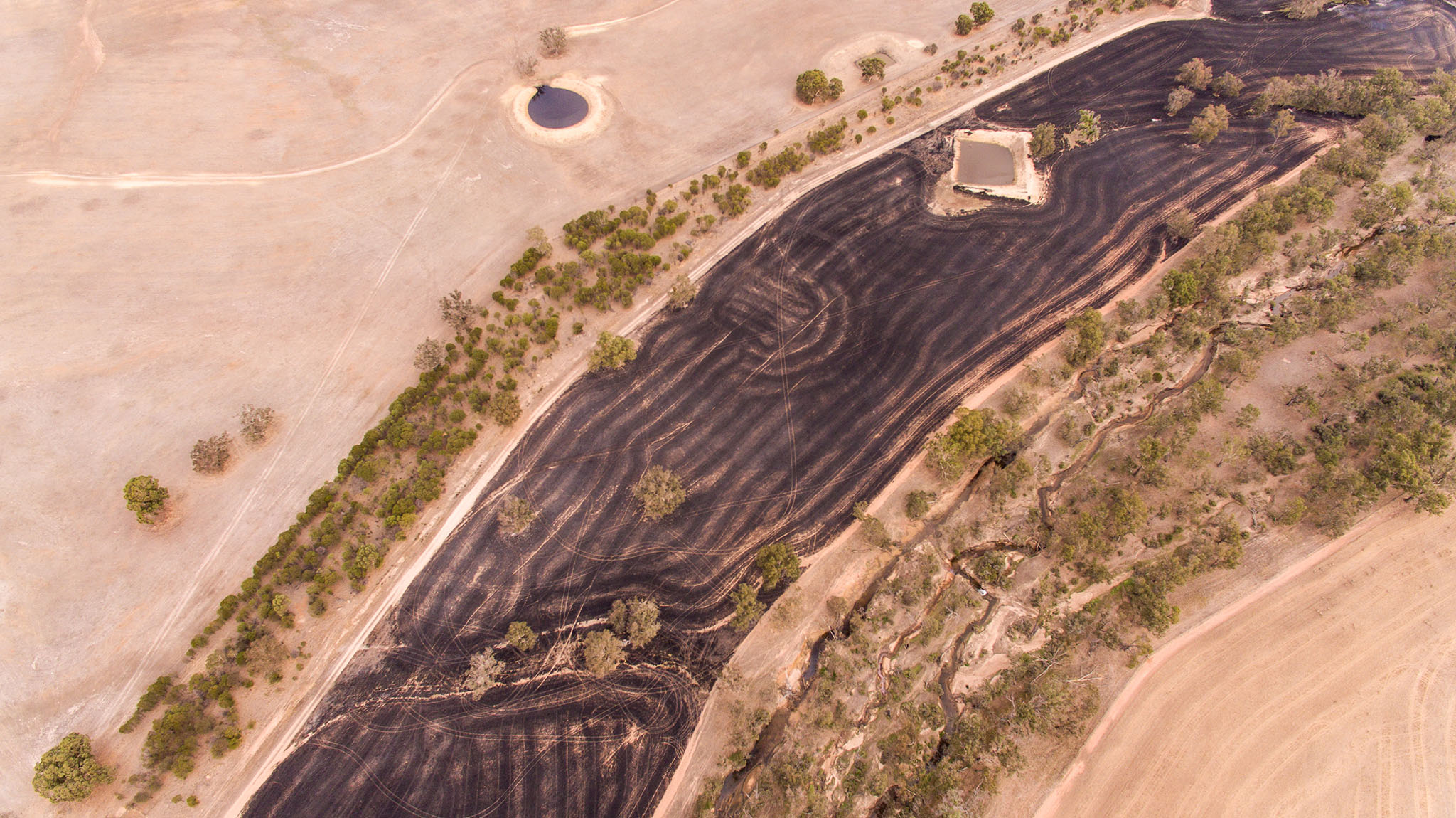 Aerial view of landscape with burnt black band arcing through the frame. Image by caro Telfer, Photographer.