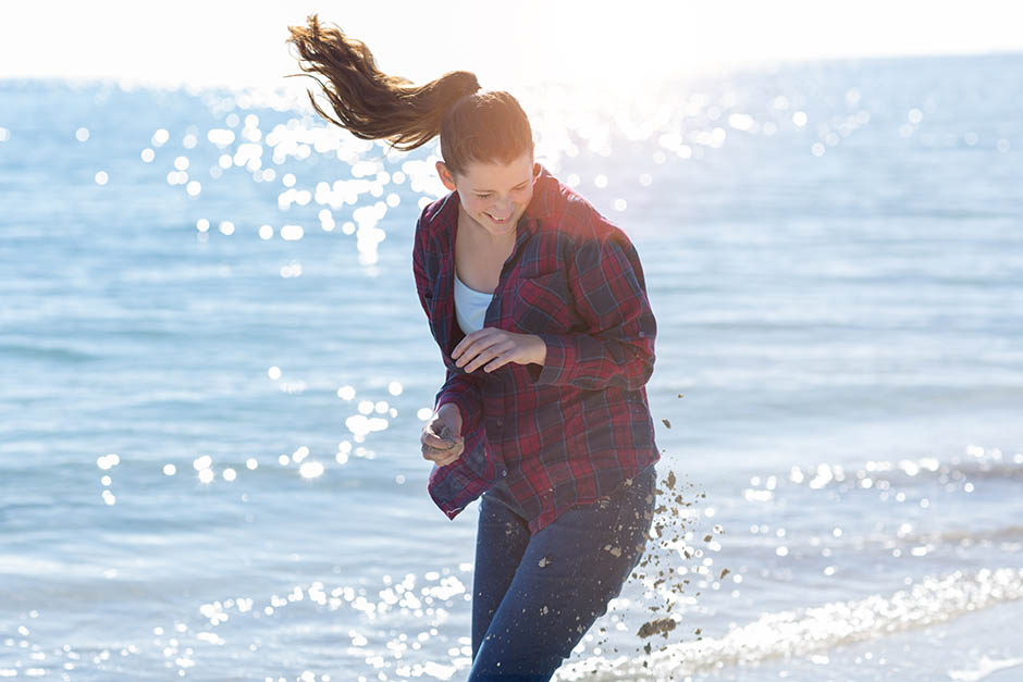 photo of teenage girl avoiding sand thrown at her on the beach. Photo by caro telfer.