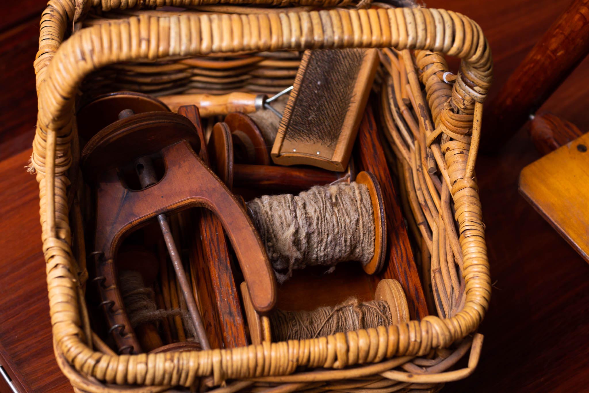 photo of cane basket containing spinning wheel accessories and spun wool. Photo by Caro Telfer.