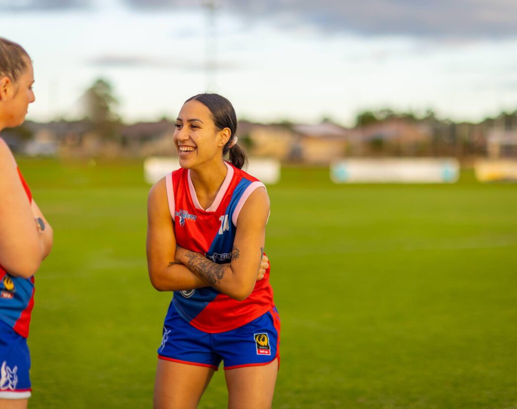 Woman football player with arms crossed laughing as she looks at another player