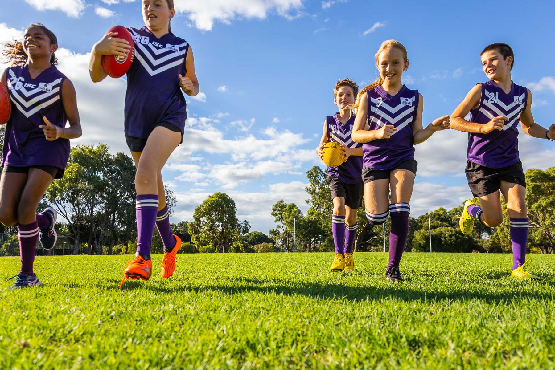 a group of schoolchildren with AFL football running towards camera, seen from a low angle.