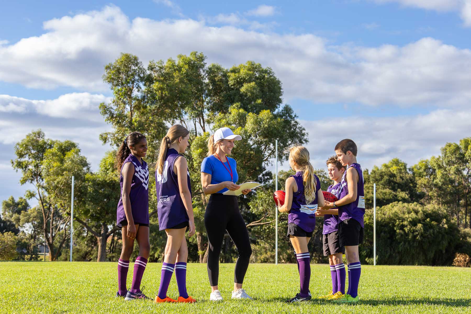 a coach addressing some kids from a football team standing in a group on football oval