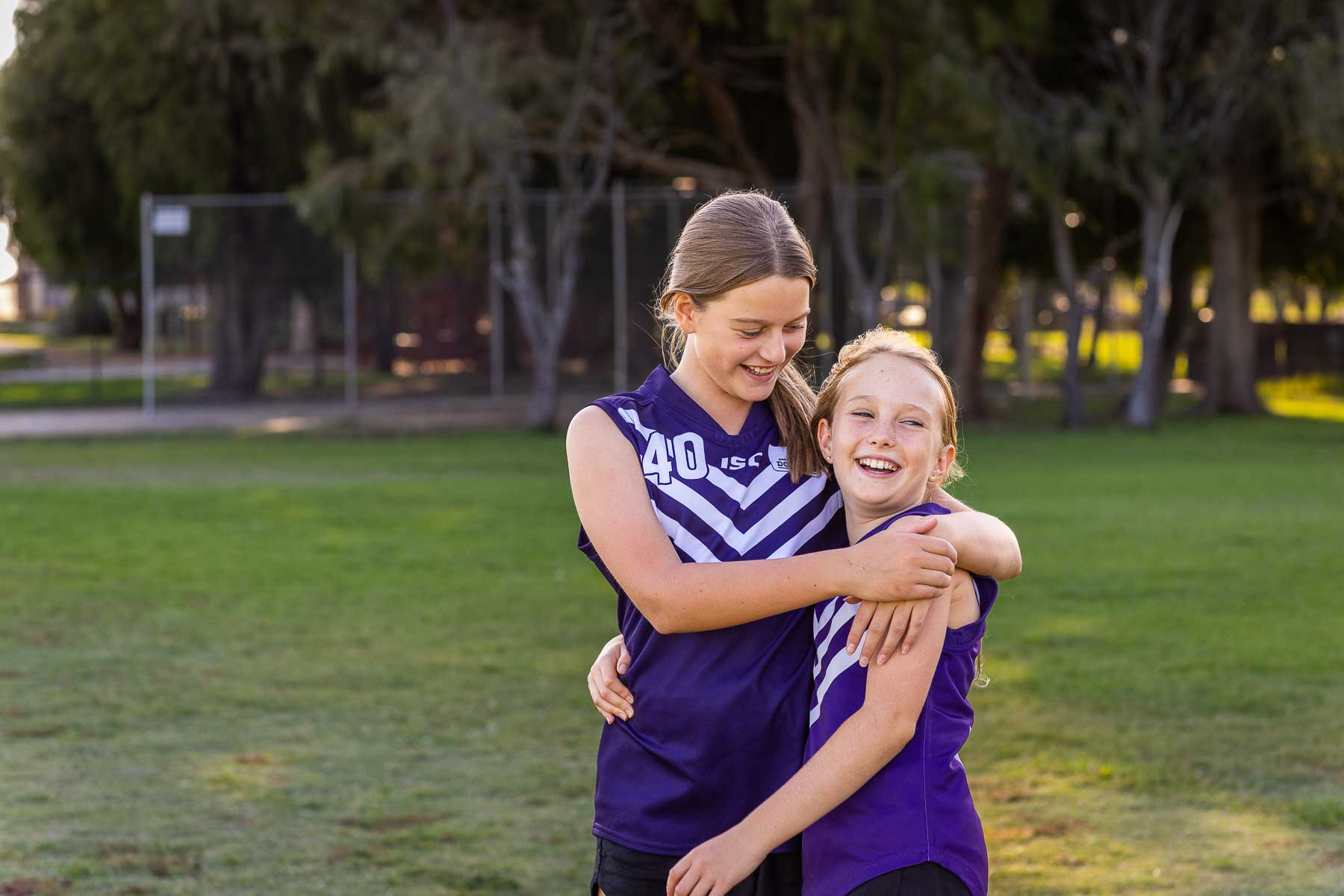 photo of two happy schoolgirls in footy jerseys with arms around each other