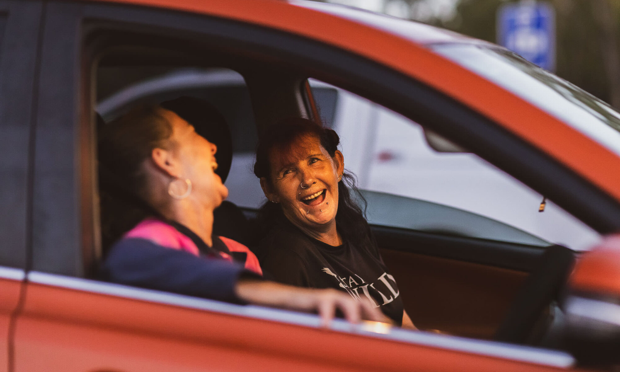 two women sitting in a red car and laughing together